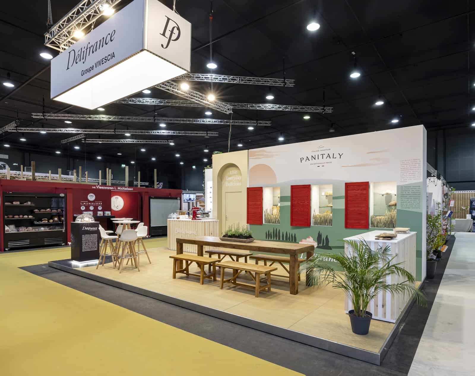 Zijaanzicht van de 'Panitaly' zone op de Délifrance stand, met een sfeervolle gevel met rode luiken en een lange houten tafel.