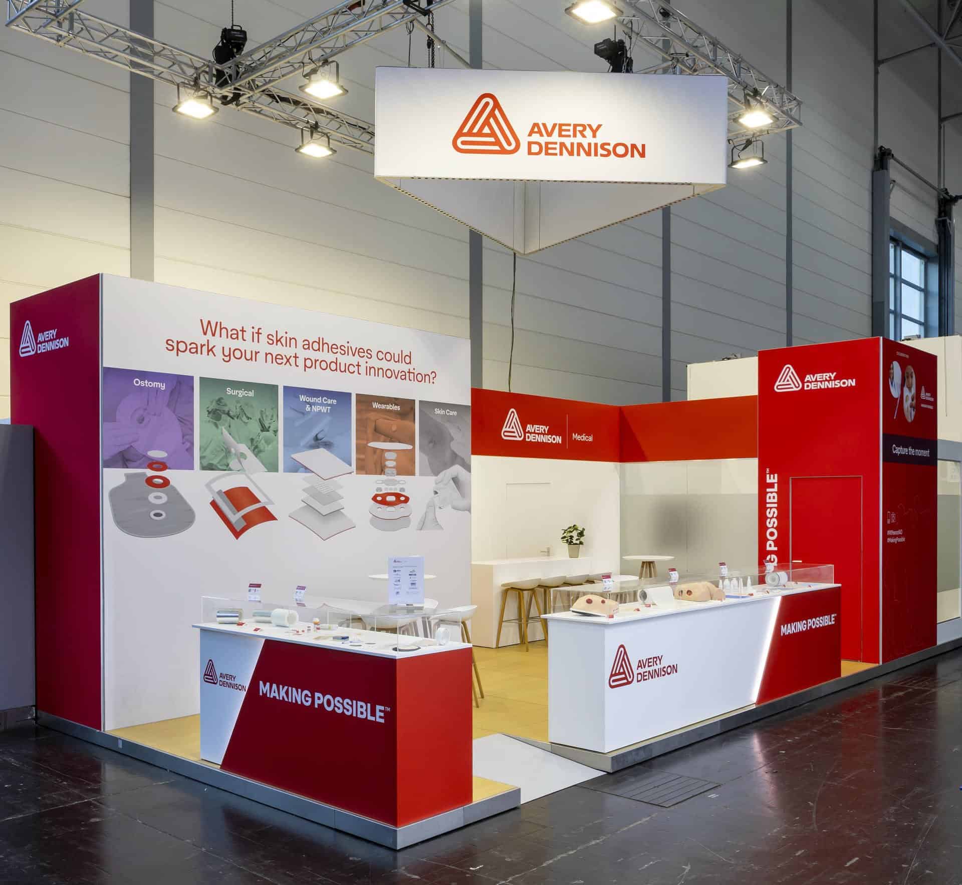 Grote, open hoekstand van Avery Dennison, gekenmerkt door strakke rode en witte houtbouw wanden, een maatwerk balie met geïntegreerde verlichting en een truss constructie met logo banner.