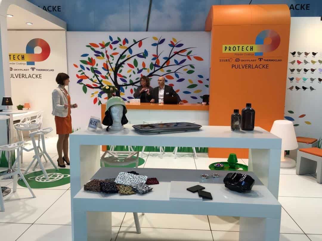 Overzicht van de Protech Group beursstand, met een grote artistieke 'kleurenboom' op de achterwand en een heldere, open inrichting.