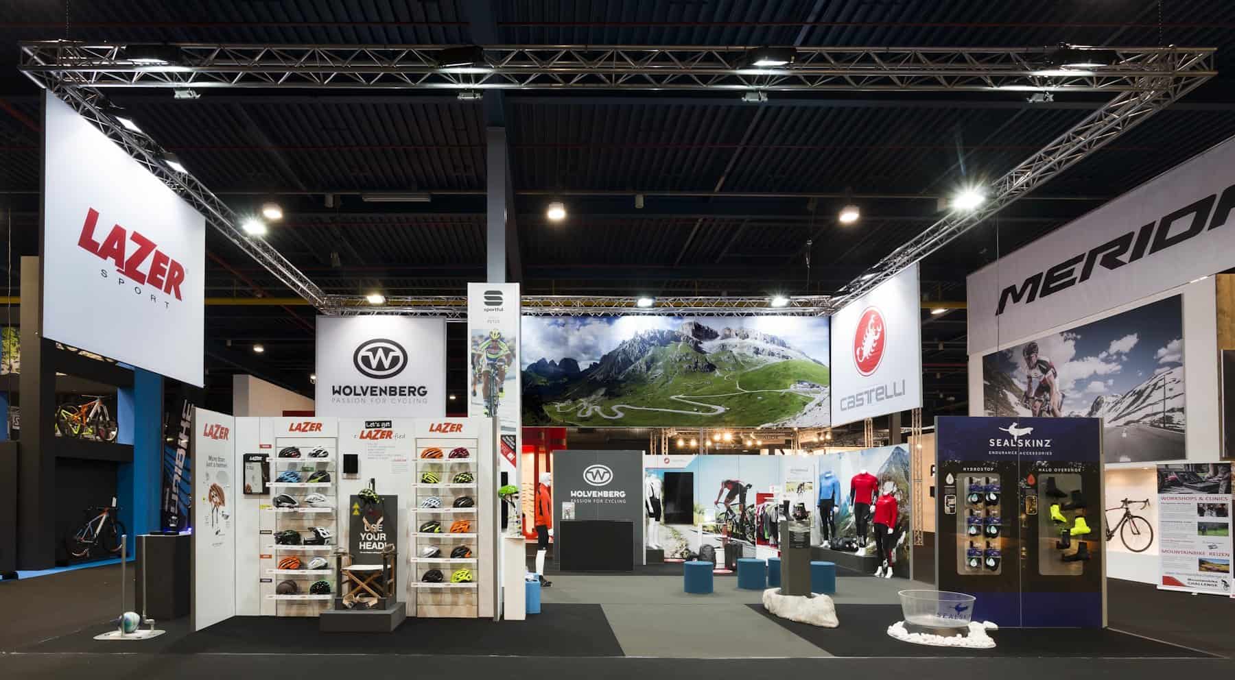 Totaaloverzicht van de grote Wolvenberg beursstand, die is ingericht als een 'shop-in-shop' met aparte zones voor merken als Lazer, Castelli en Sealskinz.