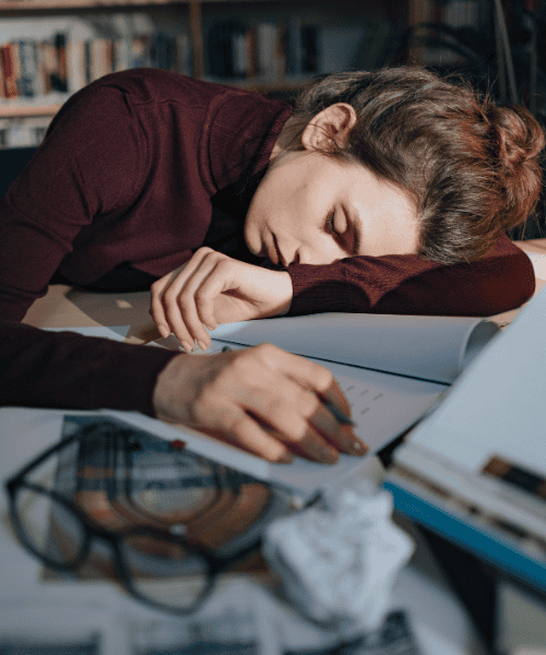 Stressed woman sitting at a desk holding her head, showing symptoms of chronic stress like fatigue and overwhelm