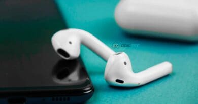 Primer plano de unos AirPods blancos junto a un smartphone, ilustrando el proceso para actualizar su firmware y mejorar su rendimiento.