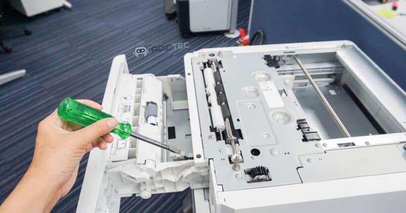 Un técnico usa un destornillador para reparar el mecanismo interno de una impresora que no imprime y necesita solución.