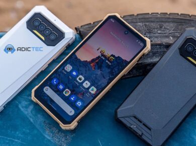 Tres smartphones resistentes de diferentes colores (blanco, beige y negro) se muestran sobre una superficie azul junto a un neumático. Los teléfonos tienen un diseño robusto y anguloso.