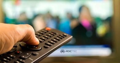 Mano sujetando un mando a distancia con una televisión desenfocada de fondo.