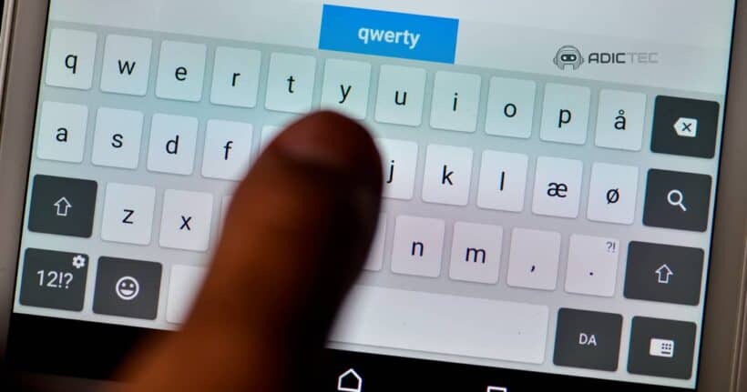 Primer plano de un dedo índice sobre un teclado QWERTY virtual en una pantalla táctil. La palabra "qwerty" se ve en la parte superior.