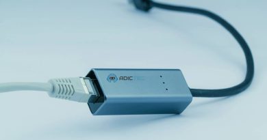 Adaptador de red USB-C a Ethernet gris, mostrando el conector USB-C y el cable Ethernet conectado.