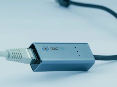 Adaptador de red USB-C a Ethernet gris, mostrando el conector USB-C y el cable Ethernet conectado.