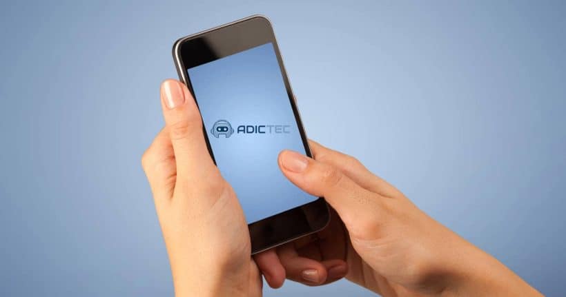 Manos sosteniendo un iPhone con la pantalla encendida, mostrando el logotipo de Adictec.
