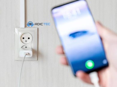 Un cargador de teléfono conectado a una toma de corriente, con un teléfono móvil desenfocado en primer plano.