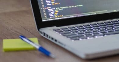 Portátil con código CSS en pantalla sobre un escritorio de madera, junto a un bolígrafo y una nota, al estudiar DAW online