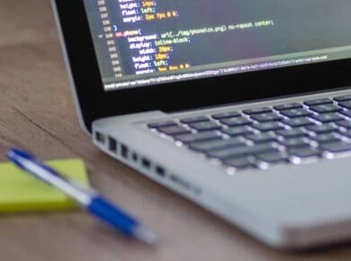 Portátil con código CSS en pantalla sobre un escritorio de madera, junto a un bolígrafo y una nota, al estudiar DAW online