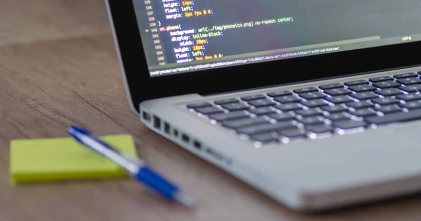 Portátil con código CSS en pantalla sobre un escritorio de madera, junto a un bolígrafo y una nota, al estudiar DAW online