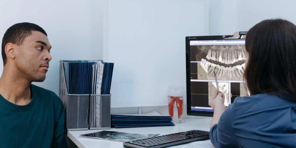 Dentist showing patient a dental X-ray result on screen.