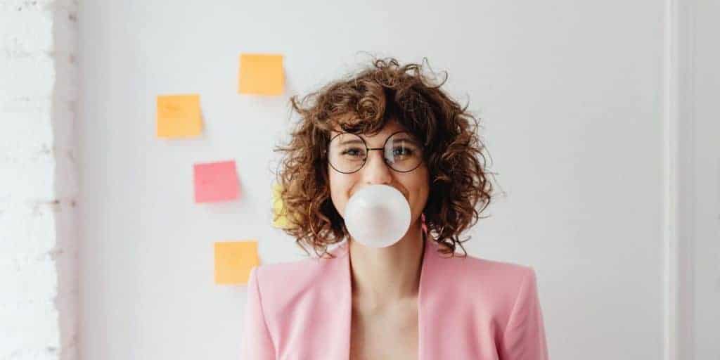 Woman in a pink corporate attire blowing a bubble gum.