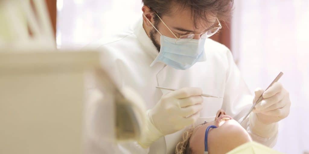 Dentist wearing mask while doing dental treatment to patient.