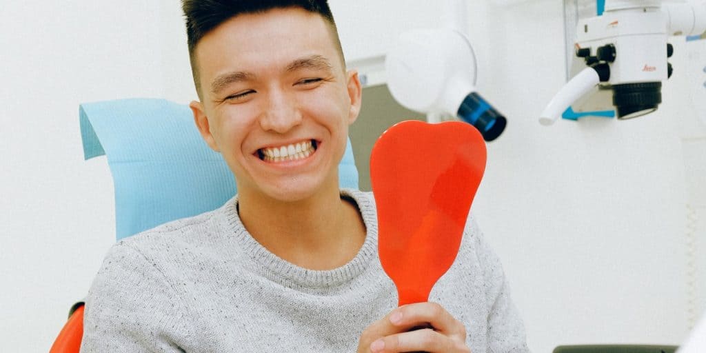 Male patient inside dental office looking in the mirror with a smile.