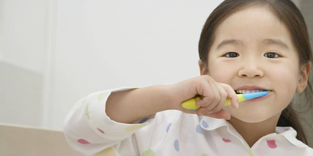 Young girl brushing teeth with toothbrush.