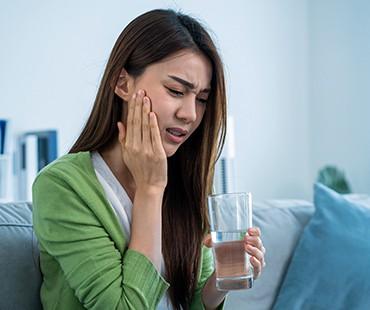 Woman with tooth pain holding a glass of water while touching cheek.