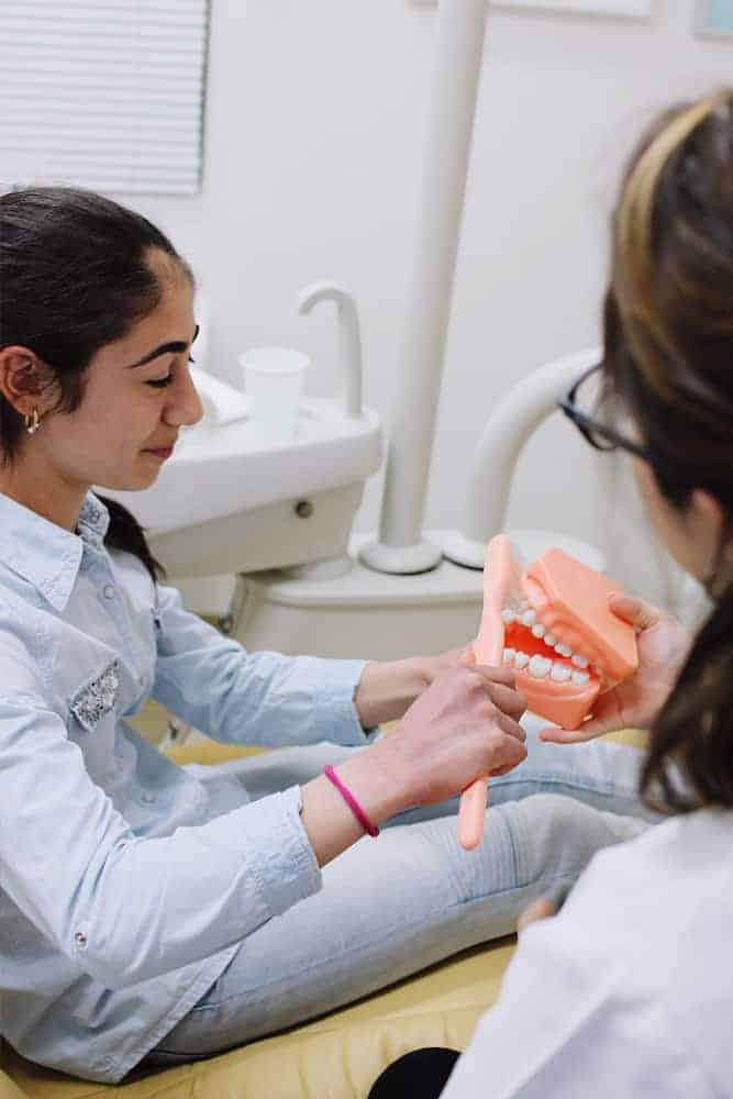 Young patient brushing the teeth model held by the dentist.