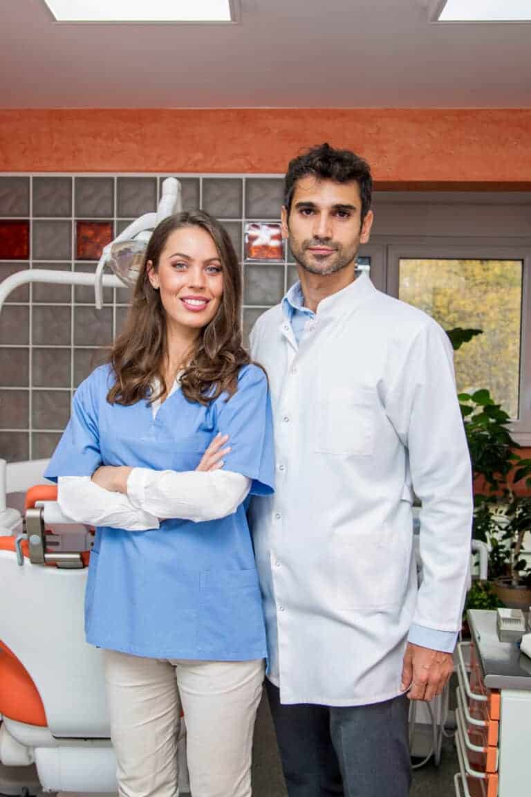 Male and female dental professionals standing inside a dental office.