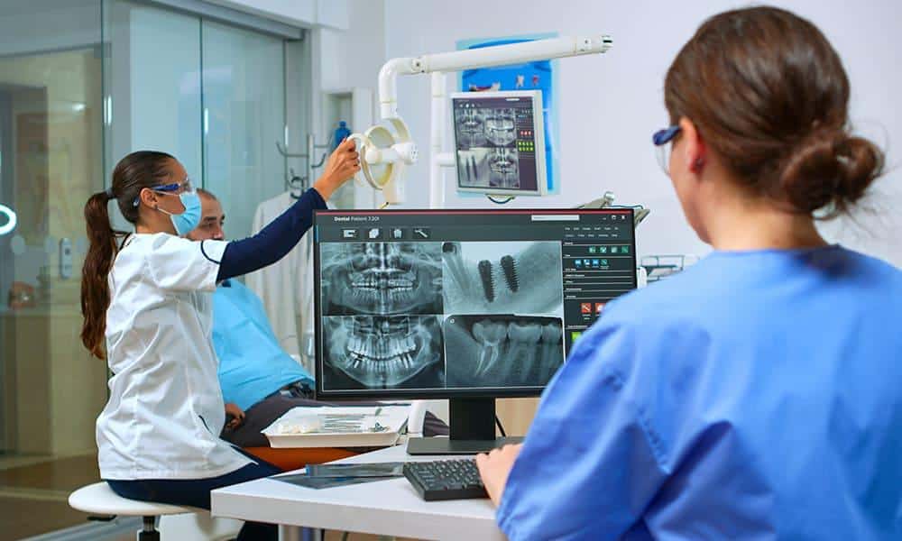 Hygienist, dentist, and patient looking at dental X-ray results.