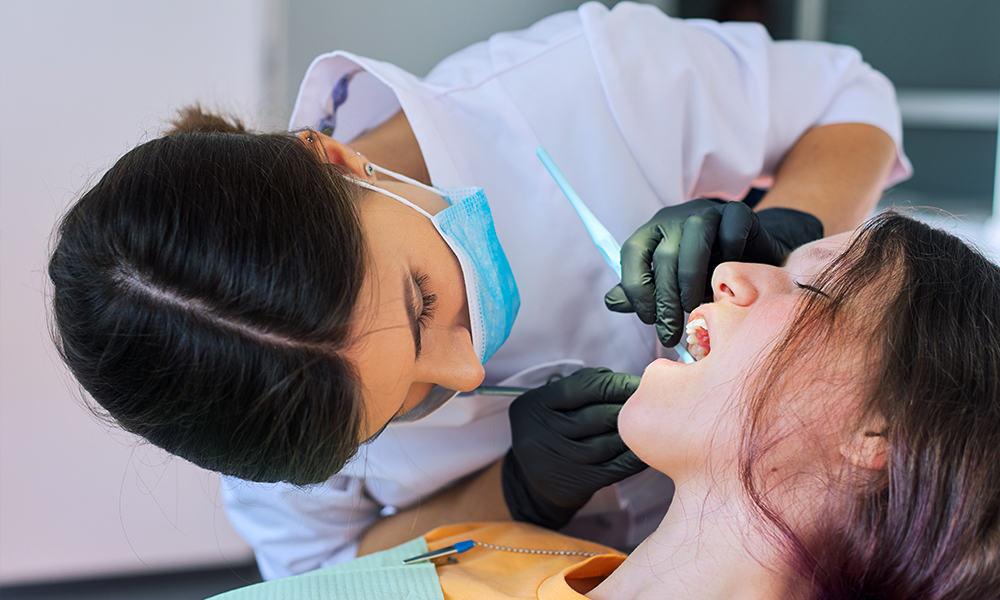 Dental professional checking teen patient's mouth using dental tool.