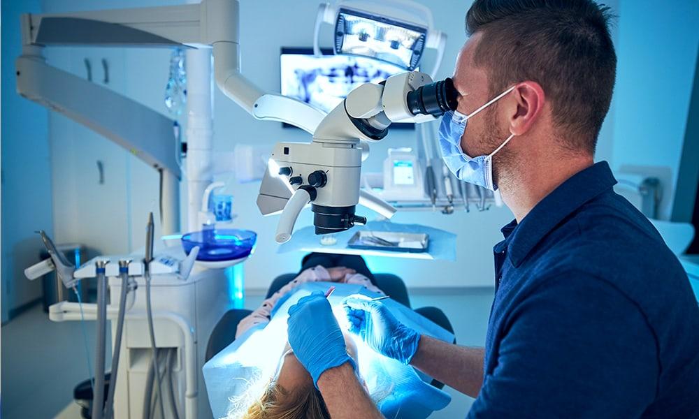 Dentist looking through modern dental microscope. Patient under pocket reduction surgery.