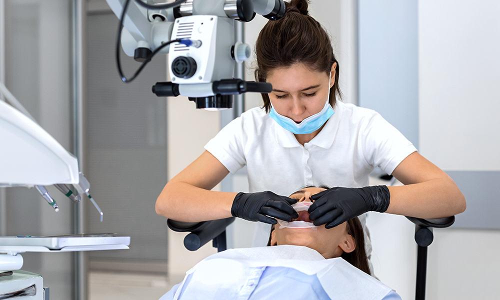 Hygienist putting disposable rubber dam on patient's mouth before regenerative procedures.