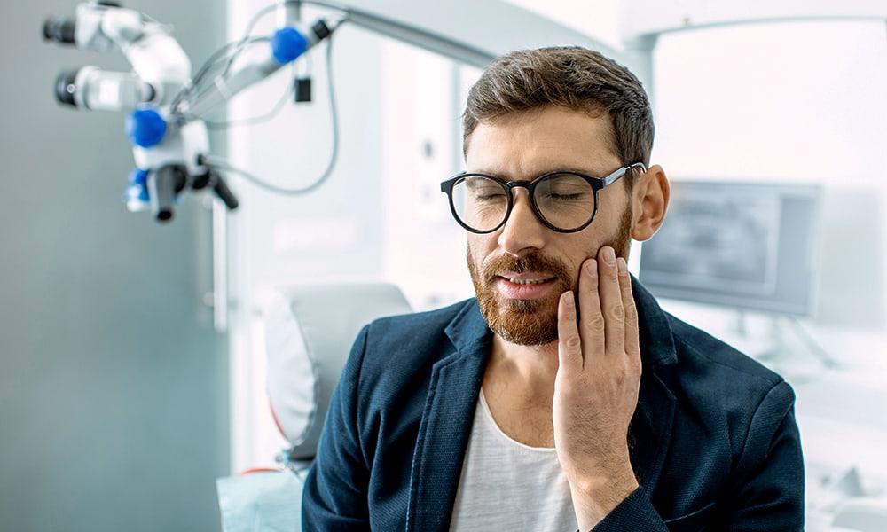 Male patient inside a dental office holding cheek in pain due to dental emergency.