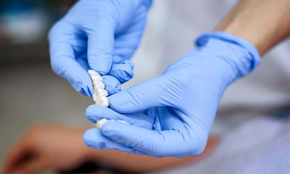 Hands with blue gloves holding porcelain fixed bridges.