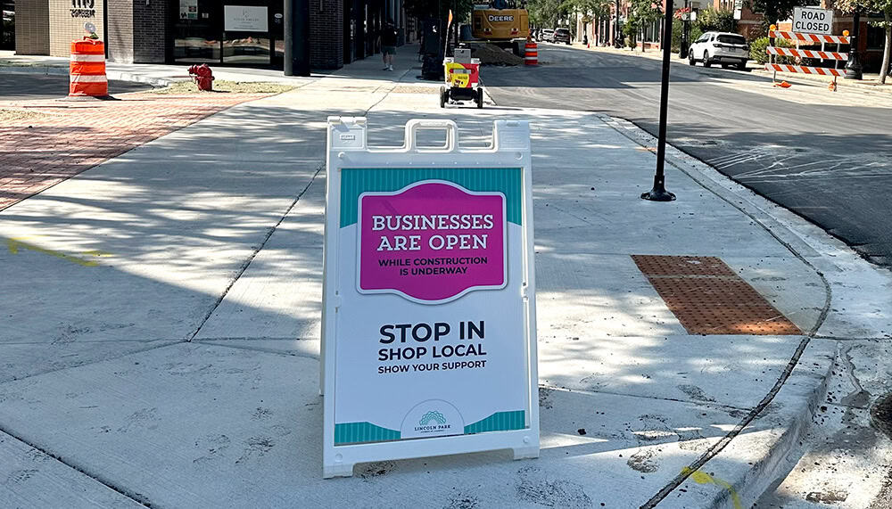 Lincoln Park Chamber of Commerce sandwich board sign reading 'Businesses Are Open, Stop In, Shop Local' on a Chicago sidewalk.