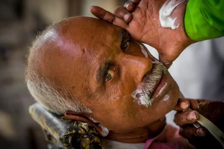 Street barber in India lathering an older man's face for a shave