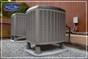 Two outdoor air conditioning units are installed on sturdy platforms beside a wood-sided building, with electrical boxes and conduit neatly arranged. With Bell Brothers’ trusted service—including our No Surprise Guarantee, background-checked technicians, upfront pricing, and outstanding reputation throughout Northern California—you can count on a worry-free experience for all your heating and cooling needs.