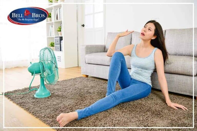 A woman sits on the floor in front of a fan, fanning herself to stay cool. The Bell Brothers logo appears in the upper left corner, highlighting their trusted service throughout Northern California. With background-checked technicians, upfront pricing, and the No Surprise Guarantee, Bell Brothers ensures every customer’s comfort and peace of mind.