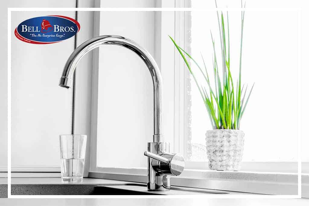 A sparkling modern kitchen sink faucet is featured alongside a glass and a potted plant on the windowsill, creating a fresh and welcoming home environment. The Bell Bros. logo appears in the upper left corner, representing Northern California’s trusted home service team. Count on Bell Brothers’ background-checked technicians, transparent upfront pricing, and No Surprise Guarantee for every service—just part of why homeowners across the region rely on their exceptional reputation.