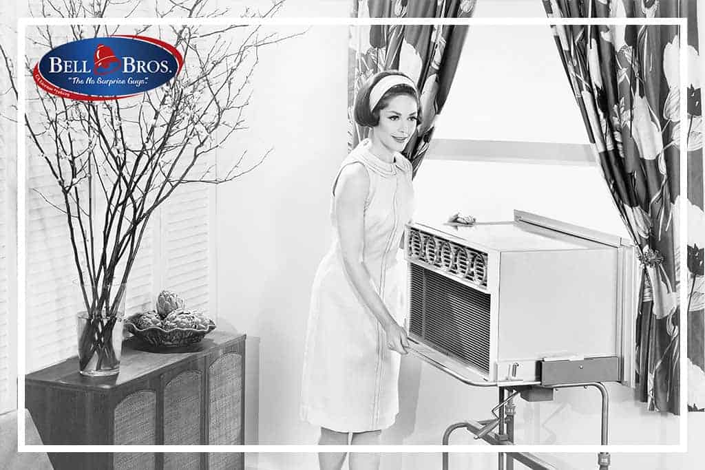 A smiling woman in a dress installs a window air conditioner in her living room, while the Bell Brothers logo appears in the top left corner. With our trusted team of background-checked technicians, No Surprise Guarantee, and clear upfront pricing, Bell Brothers delivers reliable comfort to homes across Northern California communities.