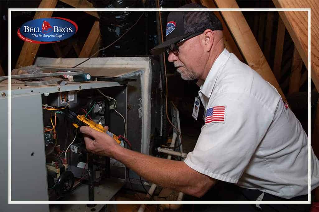 A Bell Brothers technician, clearly identified in uniform, carefully inspects the wiring of an HVAC unit in a home’s attic. The trusted Bell Bros. logo and slogan are displayed in the top left corner, highlighting their No Surprise Guarantee, upfront pricing, and extensive background checks on every technician—qualities that have earned Bell Brothers a strong reputation for reliable service throughout Northern California communities.