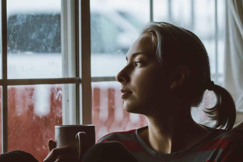 A person with a ponytail enjoys a peaceful moment indoors by a window, holding a mug and looking out at the cloudy day—confident in the comfort provided by Bell Brothers’ trusted service. With our No Surprise Guarantee, background-checked technicians, and upfront pricing, families across Northern California rely on us for dependable home solutions and peace of mind.