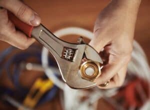 A Bell Brothers technician, fully background-checked for your peace of mind, uses an adjustable wrench to tighten a brass plumbing fitting. Various tools are visible in the softly focused background. With every service call, Bell Brothers proudly upholds their No Surprise Guarantee, providing honest, upfront pricing and the trusted expertise valued by communities throughout Northern California.