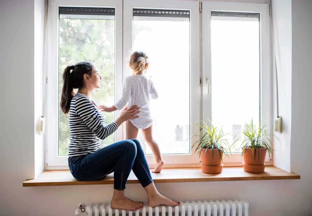 A woman and her child enjoy a peaceful moment by the window, surrounded by thriving potted plants—a reflection of the comfort and trust Bell Brothers brings to homes across Northern California. With our No Surprise Guarantee, thoroughly background-checked technicians, and upfront pricing, families just like yours count on our reputable service for total peace of mind.