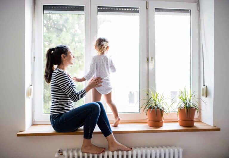 A woman and her child enjoy a peaceful moment by the window, surrounded by thriving potted plants—a reflection of the comfort and trust Bell Brothers brings to homes across Northern California. With our No Surprise Guarantee, thoroughly background-checked technicians, and upfront pricing, families just like yours count on our reputable service for total peace of mind.