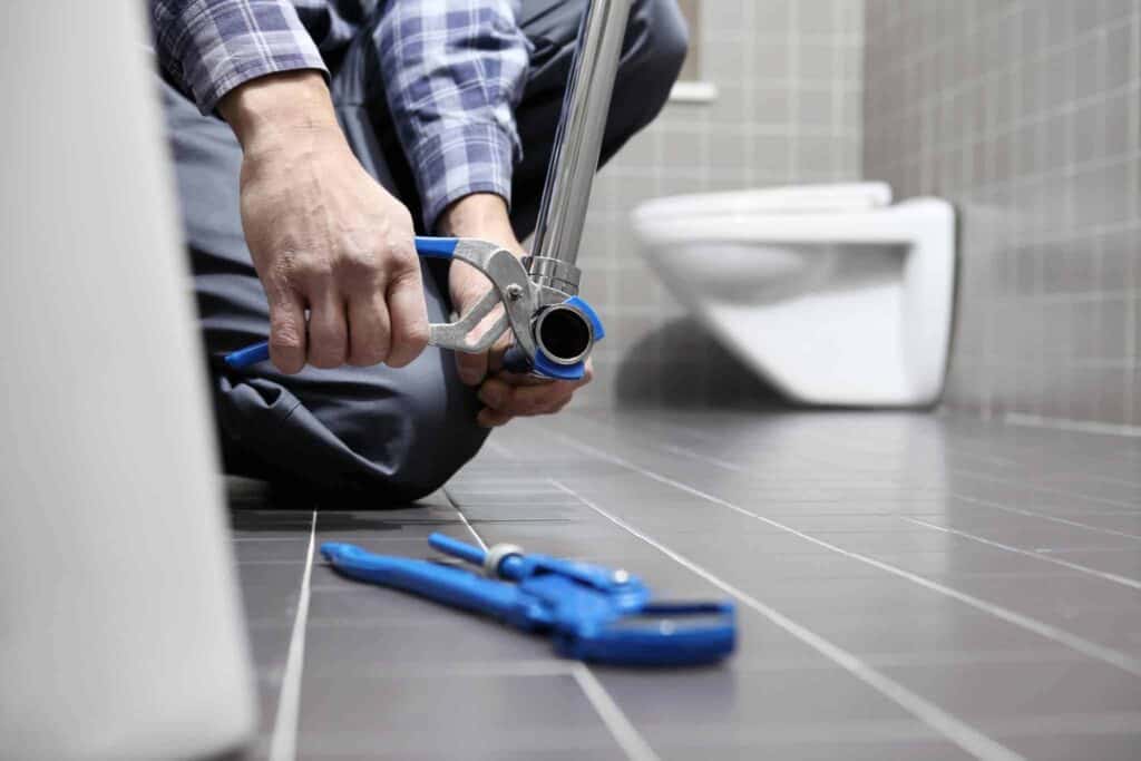 A Bell Brothers technician, thoroughly background-checked and committed to our No Surprise Guarantee, carefully tightens a bathroom pipe using professional tools. Upfront pricing and trusted service are always at the forefront as we proudly serve communities throughout Northern California. A tidy, tiled bathroom with essential tools demonstrates our dedication to quality work and reliability.