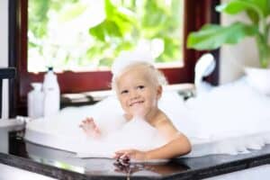 A smiling young child with blonde hair enjoys a bubble bath by a sunny window, with plants and bath products nearby—reflecting the comfort and peace of mind families feel when choosing Bell Brothers. Proudly trusted across Northern California, Bell Brothers offers upfront pricing, background-checked technicians, and our No Surprise Guarantee for reliable service you can count on.