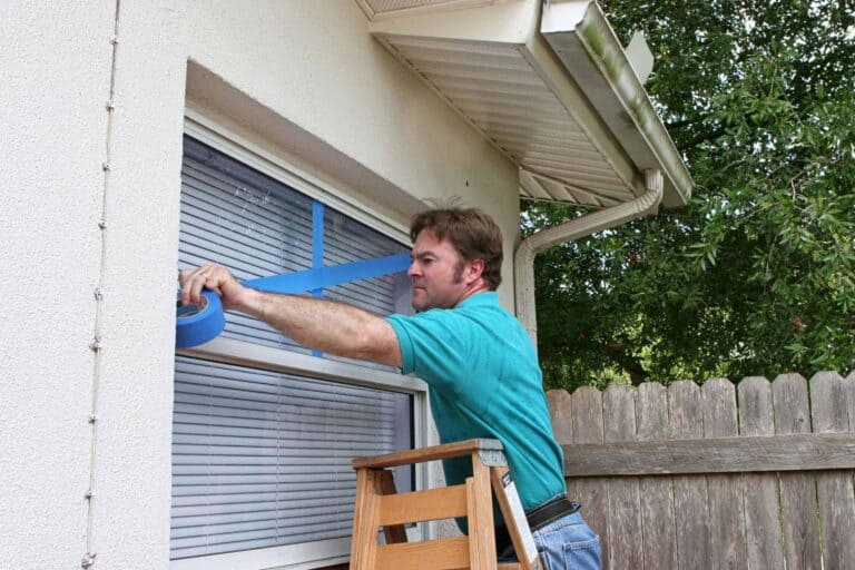 A Bell Brothers technician, fully background-checked for your peace of mind, carefully applies blue painter's tape to a home's exterior window before service. With our No Surprise Guarantee, upfront pricing, and a reputation trusted by Northern California communities, you can expect honest and dependable service every time.