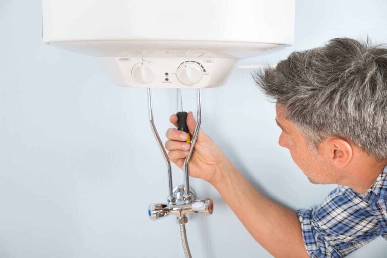 A Bell Brothers technician—background-checked for your peace of mind—uses a screwdriver to expertly service a wall-mounted water heater with clear, easy-to-read control knobs and pipes. Thanks to our No Surprise Guarantee and upfront pricing, homeowners across Northern California trust us for dependable, honest service every time.