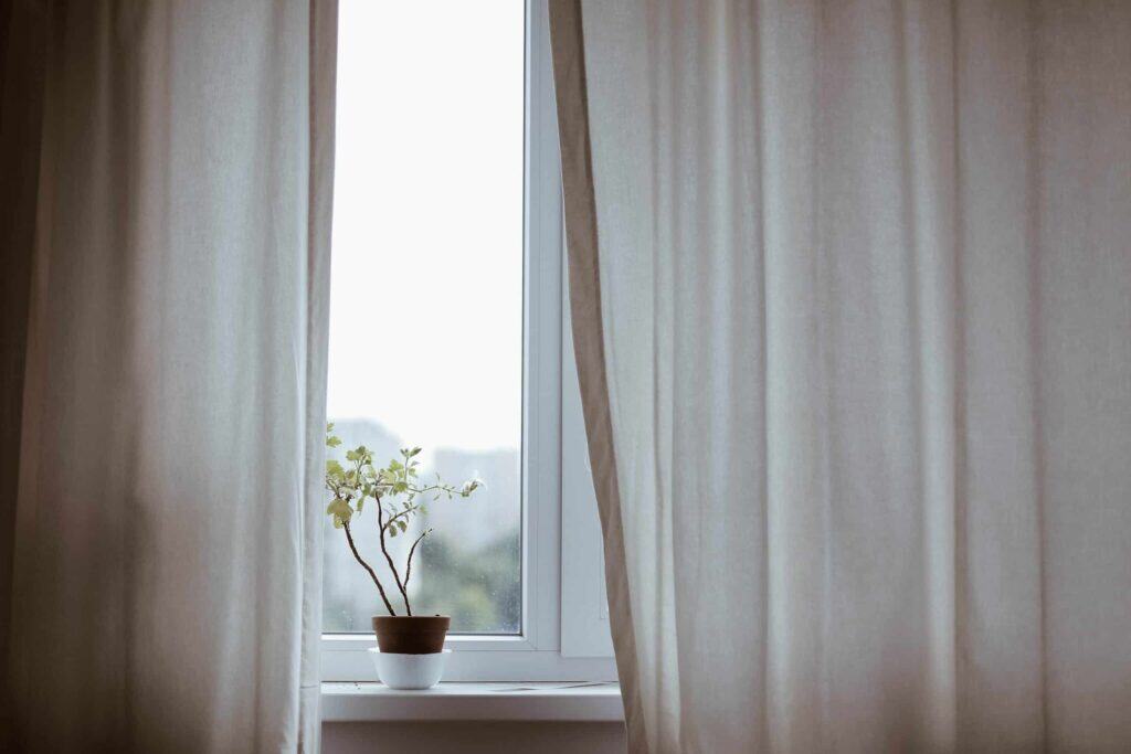 A small potted plant rests on a windowsill between partially open beige curtains, with gentle sunlight streaming in. Just as this bright space offers comfort and reassurance, Bell Brothers delivers trusted service to homes across Northern California. With our No Surprise Guarantee, upfront pricing, and thoroughly background-checked technicians, customers enjoy honest solutions from a team known for reliability in every community we serve.