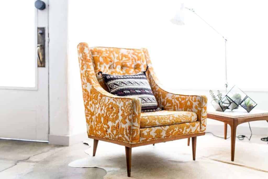 A bright, modern room featuring a stylish orange armchair with a decorative pillow, set beside a wooden table topped with a lamp and glass terrariums. Bell Brothers proudly serves Northern California communities with trusted service, including our No Surprise Guarantee, background-checked technicians, and upfront pricing for your peace of mind.