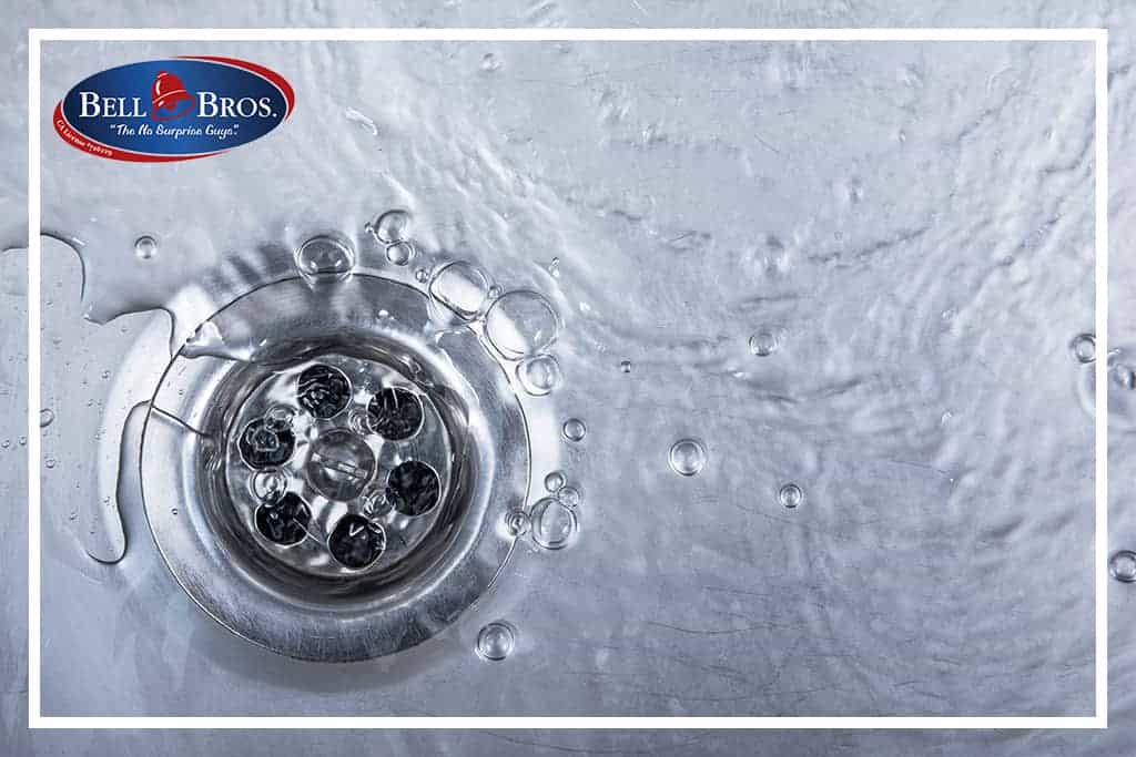 Close-up of water flowing down a stainless steel sink drain, with the Bell Bros. logo displayed in the top left corner. Trust Bell Brothers’ No Surprise Guarantee for plumbing services from background-checked technicians and enjoy upfront pricing—proudly serving communities across Northern California with a reputation for reliability.