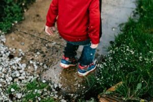 A joyful child wearing a red jacket and blue jeans splashes in a puddle along a neighborhood sidewalk surrounded by grass and gravel. At Bell Brothers, our trusted, background-checked technicians bring the same sense of happiness and reliability to homes throughout Northern California. With our No Surprise Guarantee and upfront pricing, you can count on friendly, professional service—no surprises, just great results from the team with a reputation you can trust.